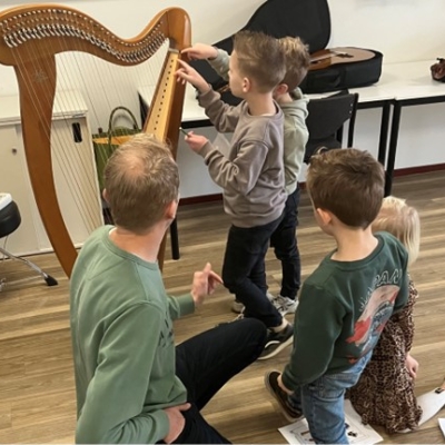 De afbeelding toont een muziekdocent en zijn leerlingen rondom een harp