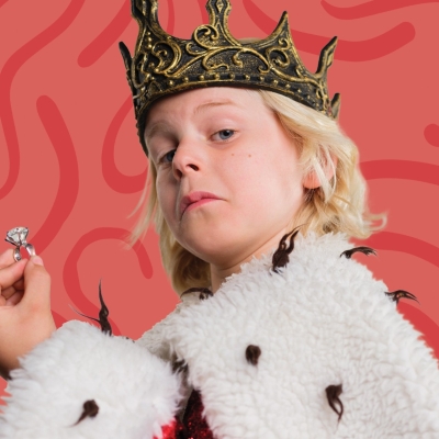 De afbeelding toont een jongetje verkleed als koning met een ring in zijn hand, een kroon op zijn hoofd, een bontjas om zijn schouders