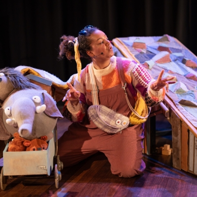De afbeelding toont een scène uit een musical met een vrouw en een olifant