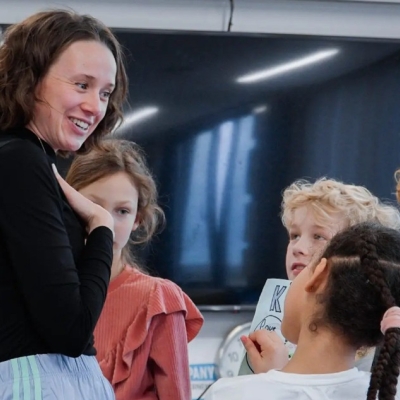 De afbeelding toont een theaterdocent met een groep kinderen