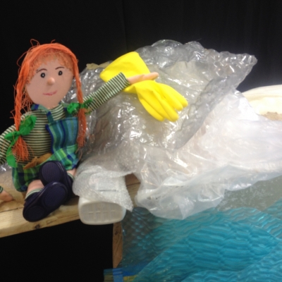 De afbeelding toont een pop (Wanda) tussen het plastic