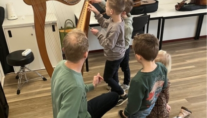 De afbeelding toont een muziekdocent en zijn leerlingen rondom een harp