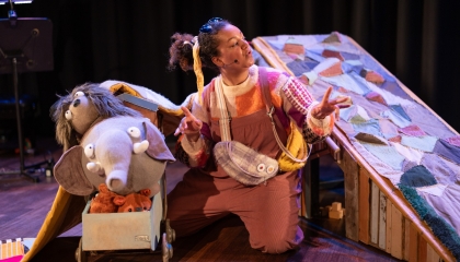 De afbeelding toont een scène uit een musical met een vrouw en een olifant