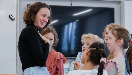 De afbeelding toont een theaterdocent met een groep kinderen