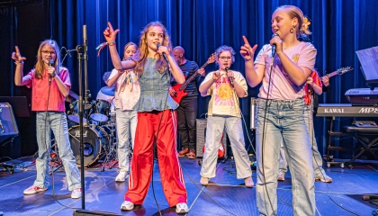 De afbeelding toont een groep kids die zingen/dansen/musical