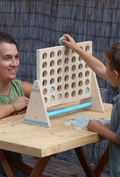 De afbeelding toont een kindje en een begeleider vier op een rij spelen